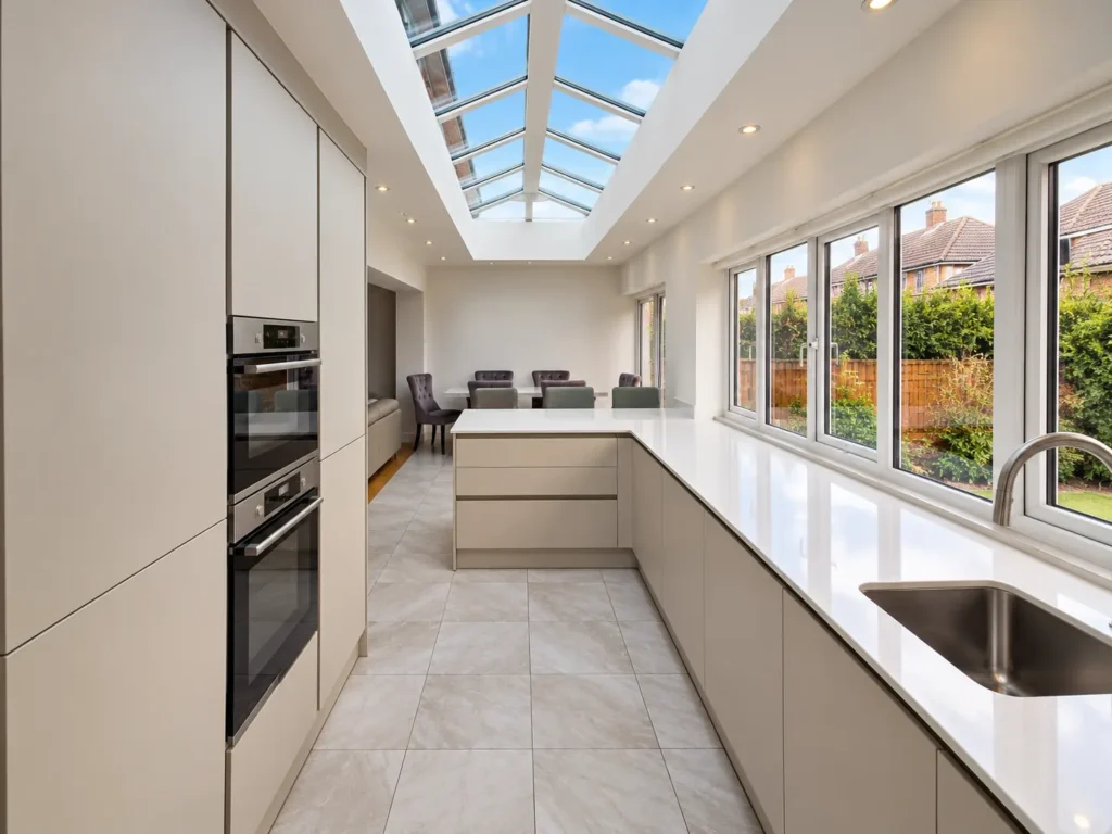 Modern kitchen extension in South Oxford featuring a glazed roof lantern, white fitted cabinetry, generous worktops and garden-facing windows.